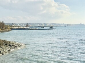 A coastal cityscape with a rocky shoreline, a pier extending into the water, and buildings in the background. - Mini Chula Inn (Chatan)