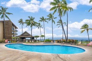 A swimming pool surrounded by palm trees, a building with a stone facade, and a view of the ocean.