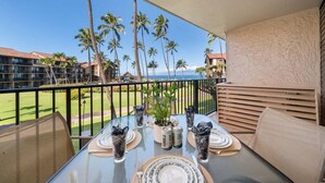 A balcony with a table set for dining, overlooking a golf course and palm trees. - SUMMER SALE! Updated 1BR Unit with Pool and Hot Tub Sleeps 4 - Papakea  B201 (Lahaina)
