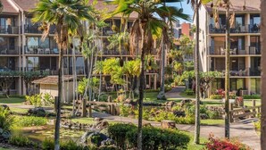 A hotel with multiple balconies, palm trees, and a landscaped garden with a pond. - SUMMER SALE! Updated 1BR Unit with Pool and Hot Tub Sleeps 4 - Papakea  B201 (Lahaina)