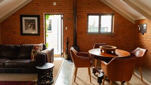 A cozy loft with a brick wall, a dining area with a round table and chairs, a sofa, and a fireplace. - Twin Rivers Bed and Breakfast (Centurion)