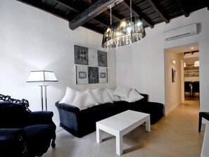 Una sala moderna con un sofá negro, una mesa de centro blanca y una araña. Se observan obras de arte abstracto en la pared y una lámpara.