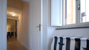 A hallway with a white door, a black and white striped cabinet, and a window with blinds. - Ripa 1 Apartment (Rome)