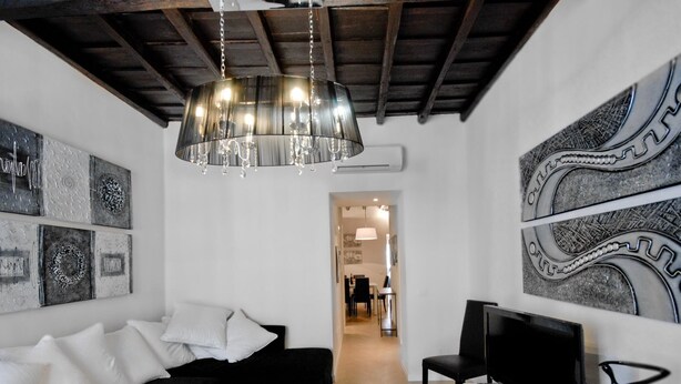 A modern living room with a black sofa, a white coffee table, and a TV on a white dresser. There are abstract wall art pieces and a chandelier. - Ripa 1 Apartment (Rome)