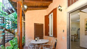 Un patio con una mesa redonda y cuatro sillas, contraventanas de madera y una escalera con plantas.