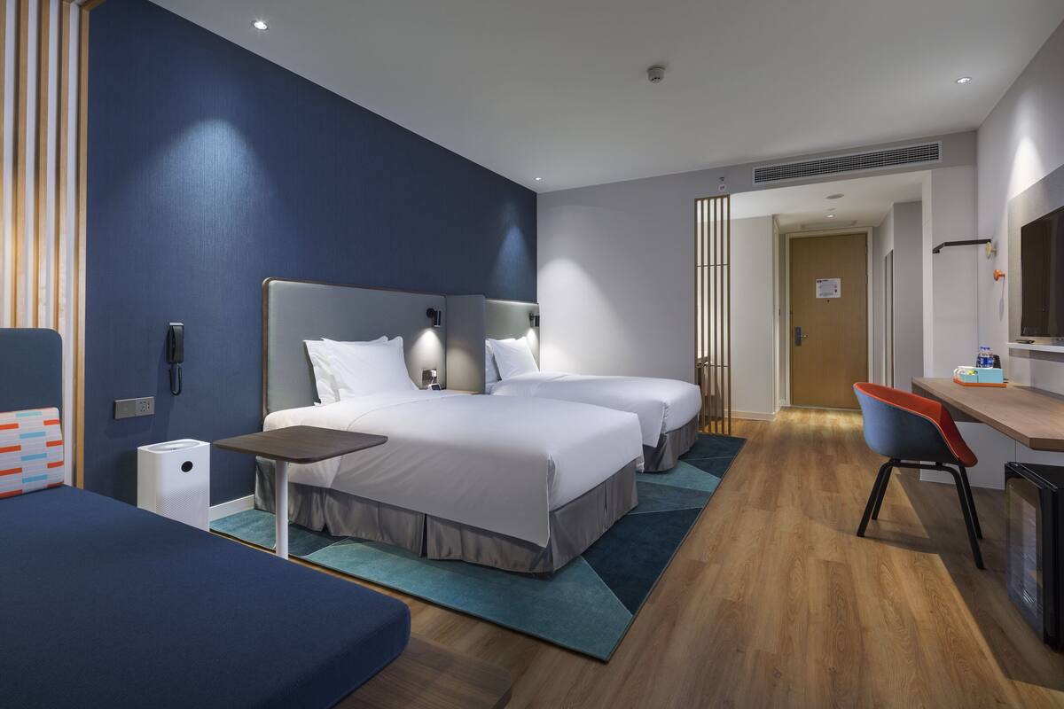 A modern hotel room with two beds, a desk, and a chair.