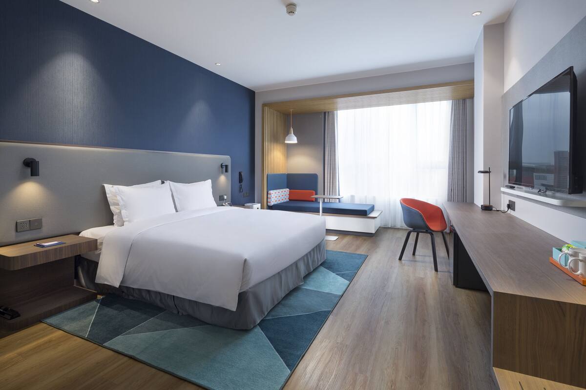 A modern hotel room with a large bed, a desk, a chair, and a TV.