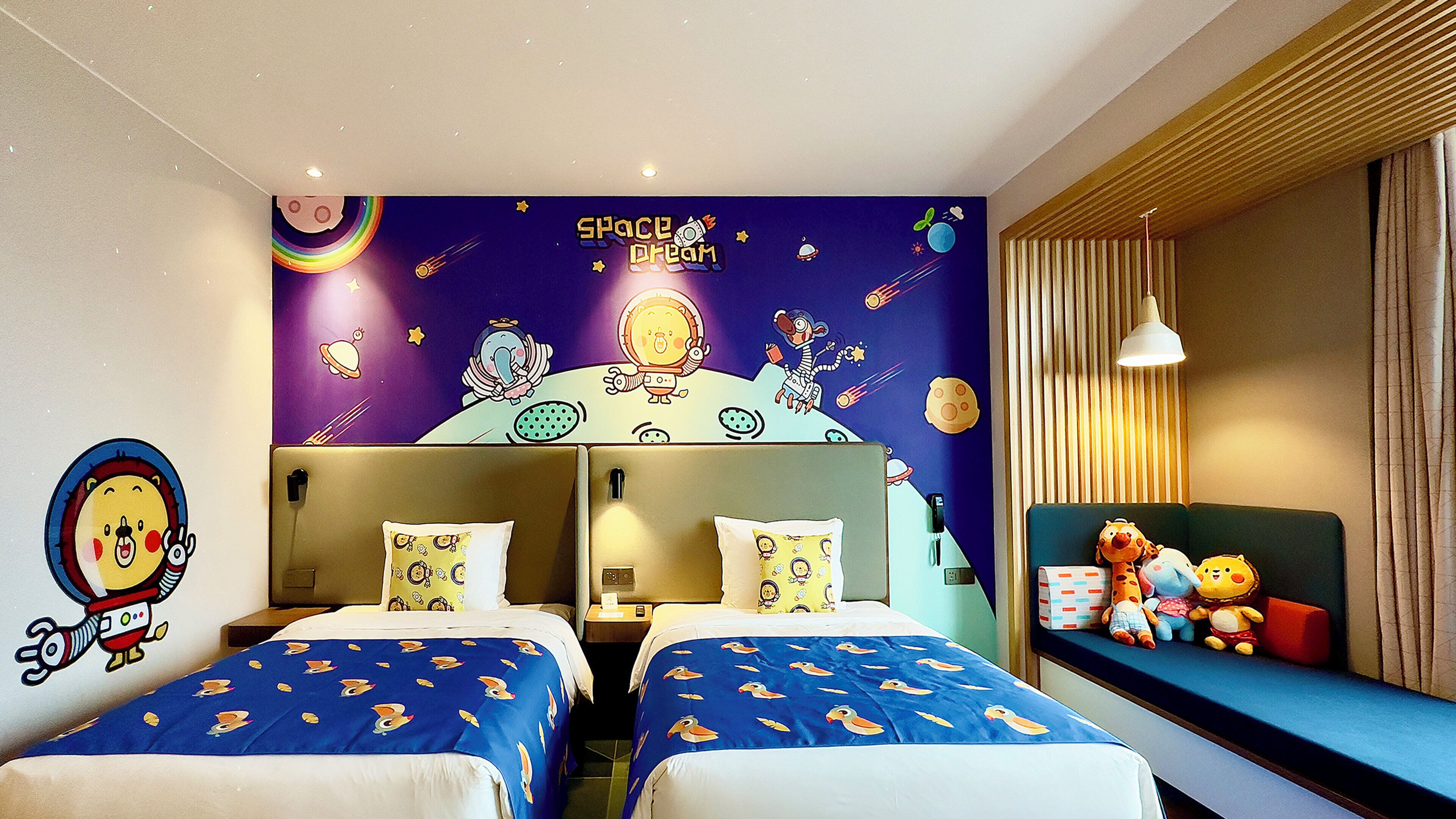 A room with two beds, a mural with space-themed artwork, and a window with curtains.