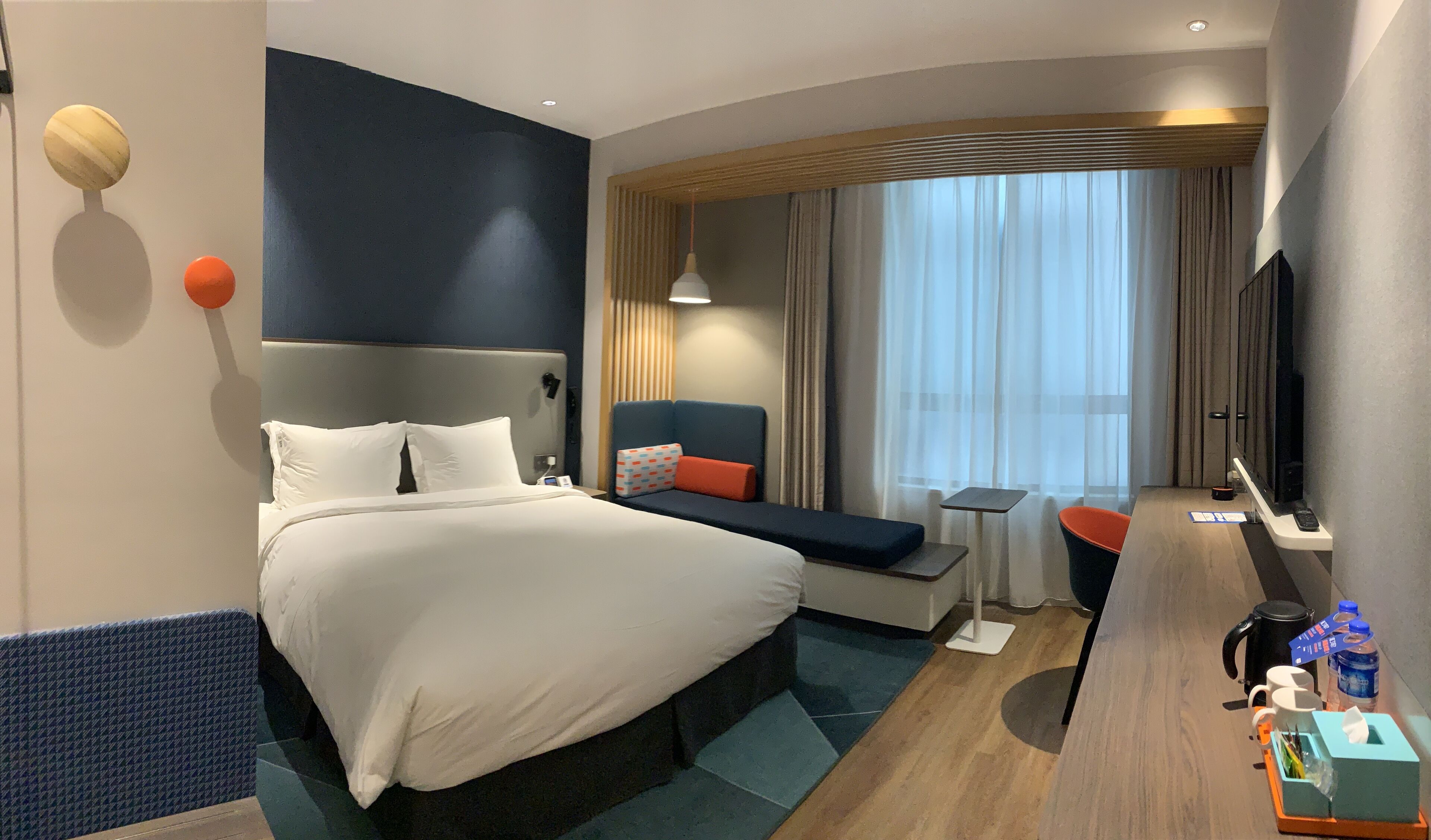 A hotel room with a large bed, a desk, a chair, and a TV.