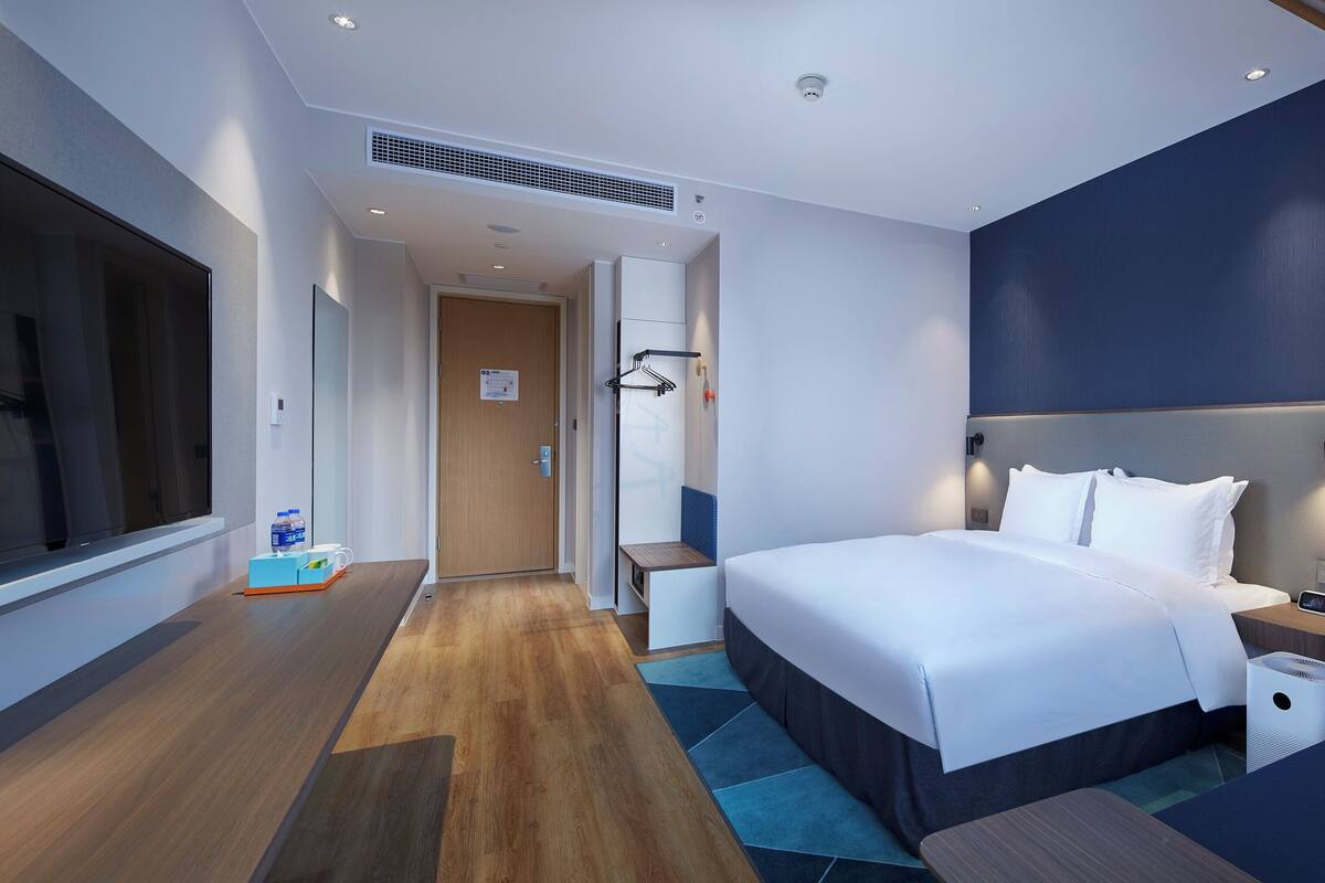 A modern hotel room with a large bed, bedside tables, a TV, and a bathroom with a shower and towel rack.