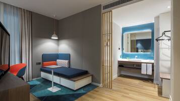 A modern hotel room with a bed, a desk, a chair, a bathroom with a mirror and sink, and a view of the outside.