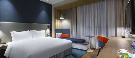 A modern hotel room with a large bed, a desk with a chair, a television, and a window with curtains.