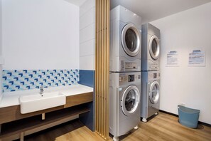 A laundry area with two front-loading washing machines, a sink, and a blue patterned wall. - Holiday Inn Express Shanghai Kangqiao by IHG (Shanghai)