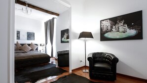Un dormitorio moderno con una cama, un sillón de cuero negro, una lámpara de pie y un cuadro grande de una fuente.