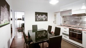 Una cocina moderna con electrodomésticos de acero inoxidable, un comedor con mesa de vidrio y un pasillo decorado con obras de arte.