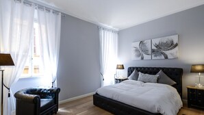 A bedroom with a large bed, a chair, and two bedside tables. - Belsiana Apartment (Rome)