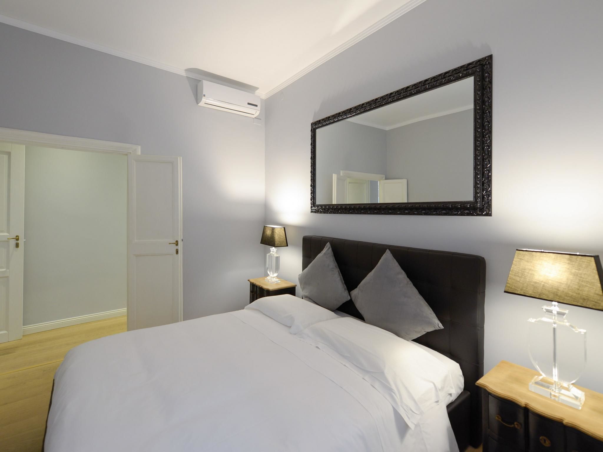 Een hotelkamer met een groot bed, een nachtkastje met een lamp, een spiegel en een airconditioning.