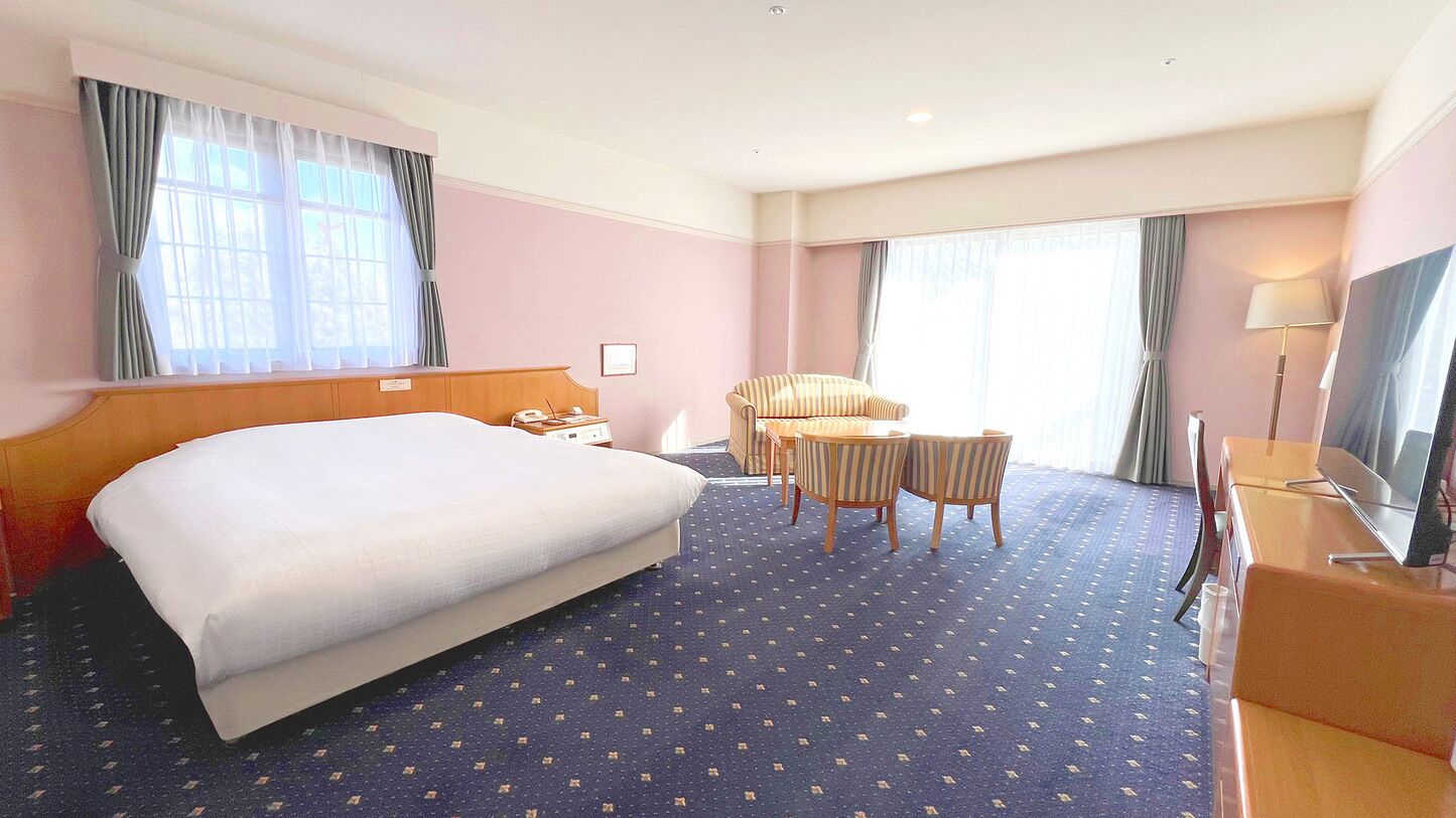 A hotel room with a large bed, a desk with a chair, a television, and a window with curtains.