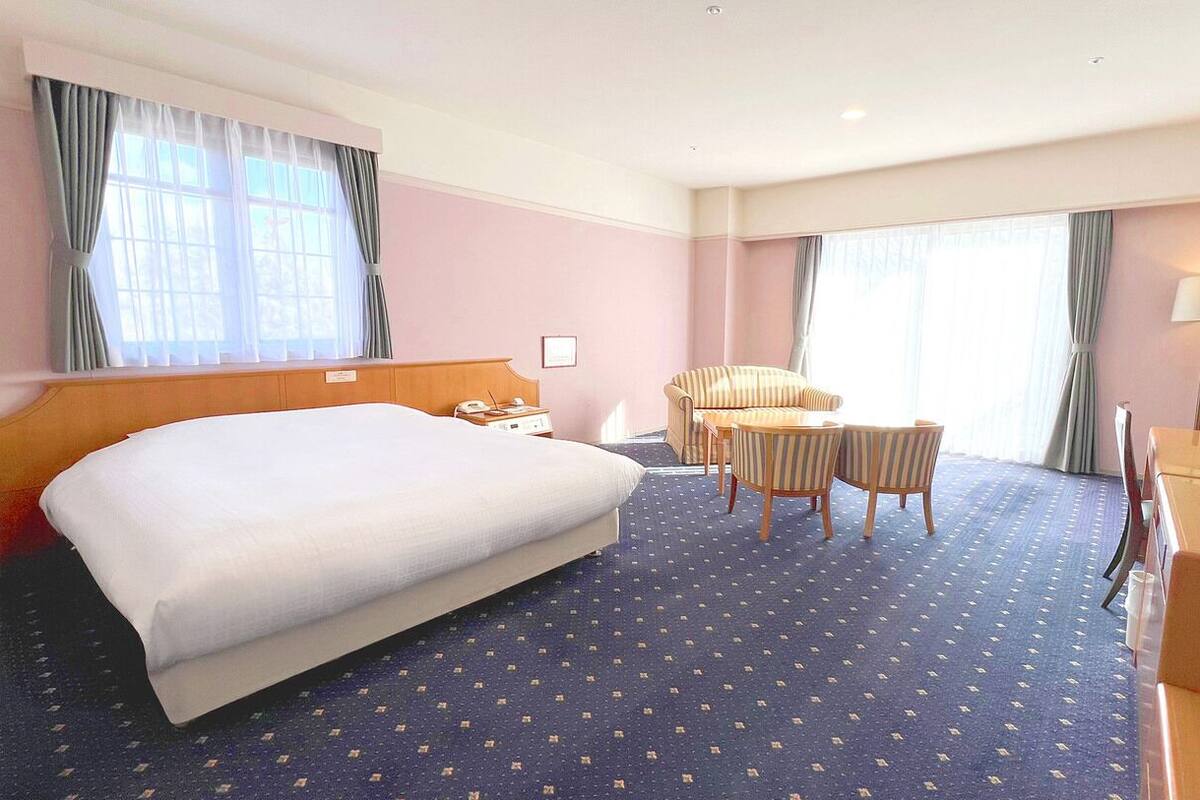 A hotel room with a large bed, a desk with a chair, a television, and a window with curtains.