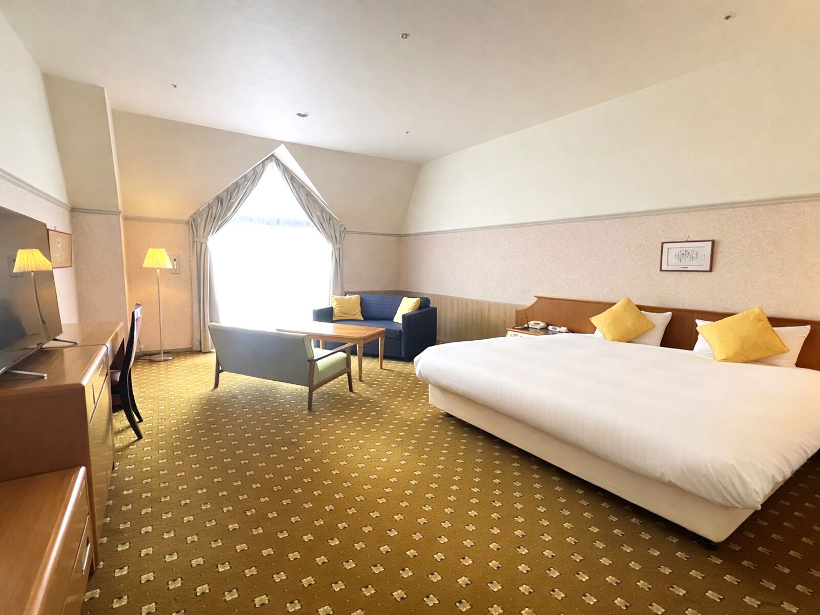 A hotel room with a bed, a desk, a chair, a sofa, and a lamp.