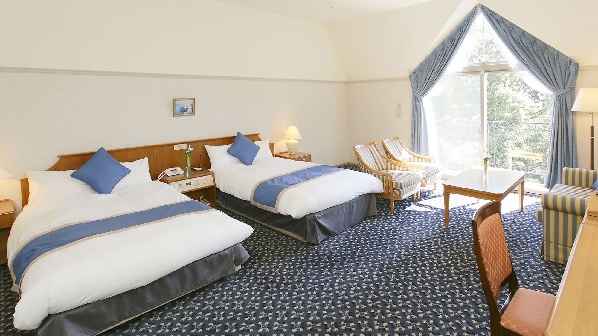 A hotel room with two beds, a desk, a chair, and a large window.