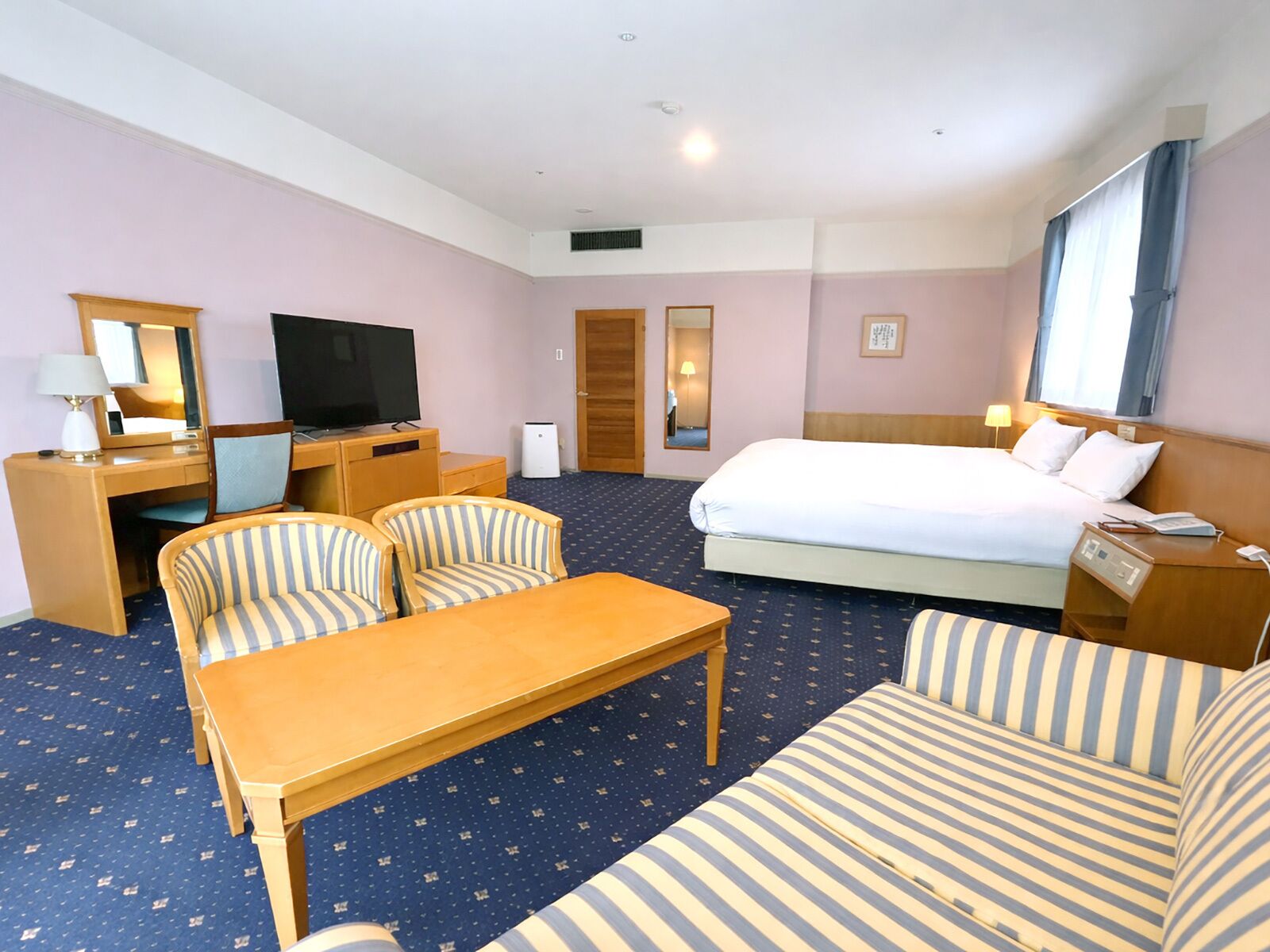 A hotel room with a bed, a desk, a television, a chair, a sofa, and a small table.