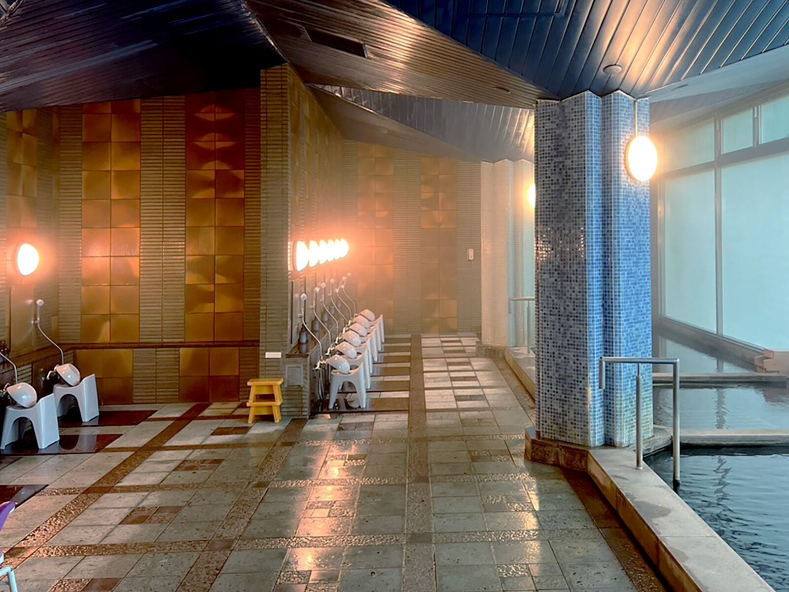 A swimming pool area with tiled flooring, benches, and a wall with a geometric pattern.
