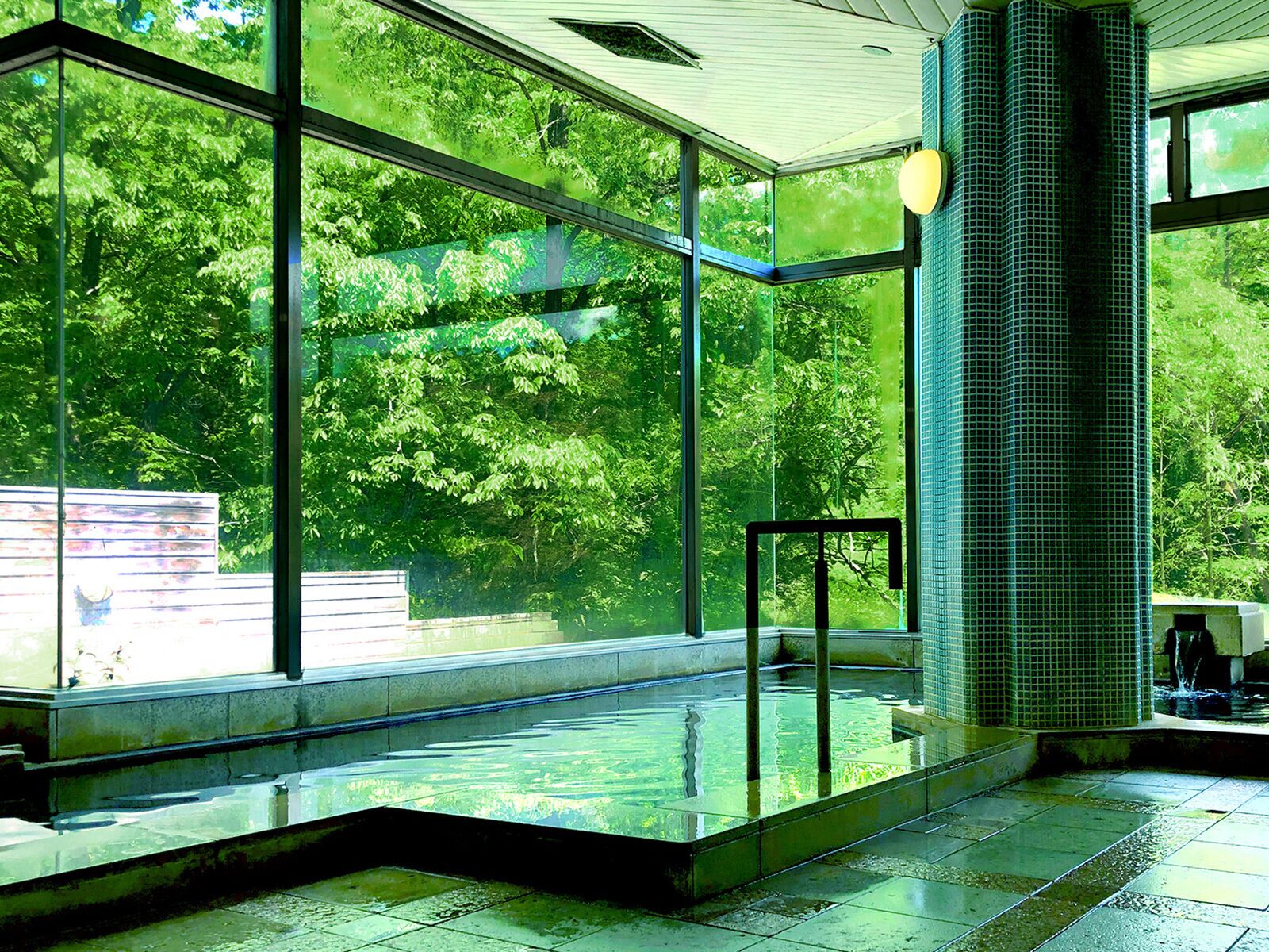 Una piscina interior moderna con ventanas amplias, barandilla de cristal y pared de azulejos.