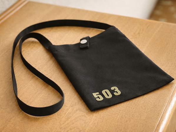 Una bolsa de mano negra con el número 503, sobre una superficie de madera.