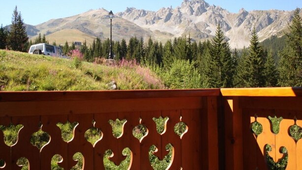A mountainous landscape with a white vehicle parked on a grassy slope, a wooden fence with heart-shaped cutouts, and a street lamp in the foreground. - Rustic apartment in Courchevel, near slopes (Courchevel 1850)