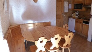 A wooden dining table with four chairs, a kitchen area with wooden cabinets, a microwave, and a small refrigerator. - Rustic apartment in Courchevel, near slopes (Courchevel 1850)
