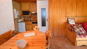 A cozy kitchen with wooden cabinets, a microwave, and a refrigerator. There's a dining table with chairs and a bowl. A wooden bench with pillows is in the corner. - Rustic apartment in Courchevel, near slopes (Courchevel 1850)