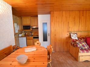 A cozy kitchen with wooden cabinets, a microwave, and a refrigerator. There's a dining table with chairs and a bowl. A wooden bench with pillows is in the corner. - Rustic apartment in Courchevel, near slopes (Courchevel 1850)