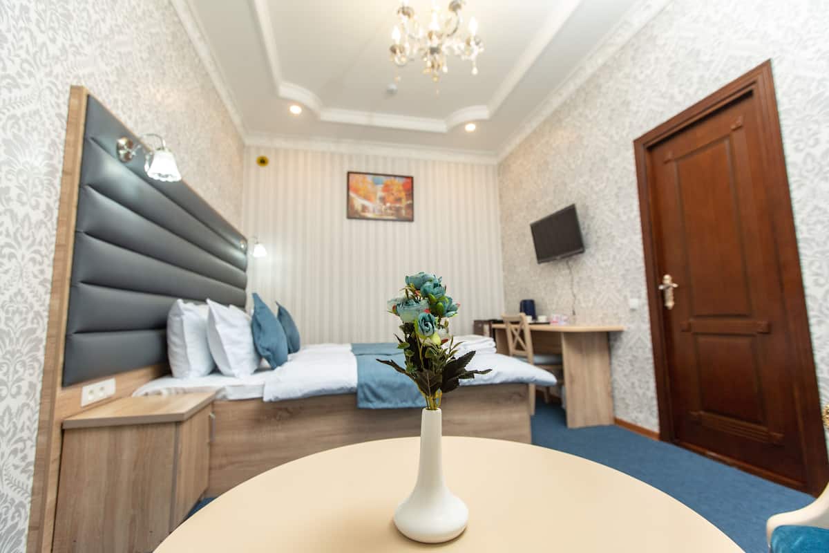 Une chambre d’hôtel avec un lit, une table de chevet, une commode, un téléviseur fixé au mur et une porte.