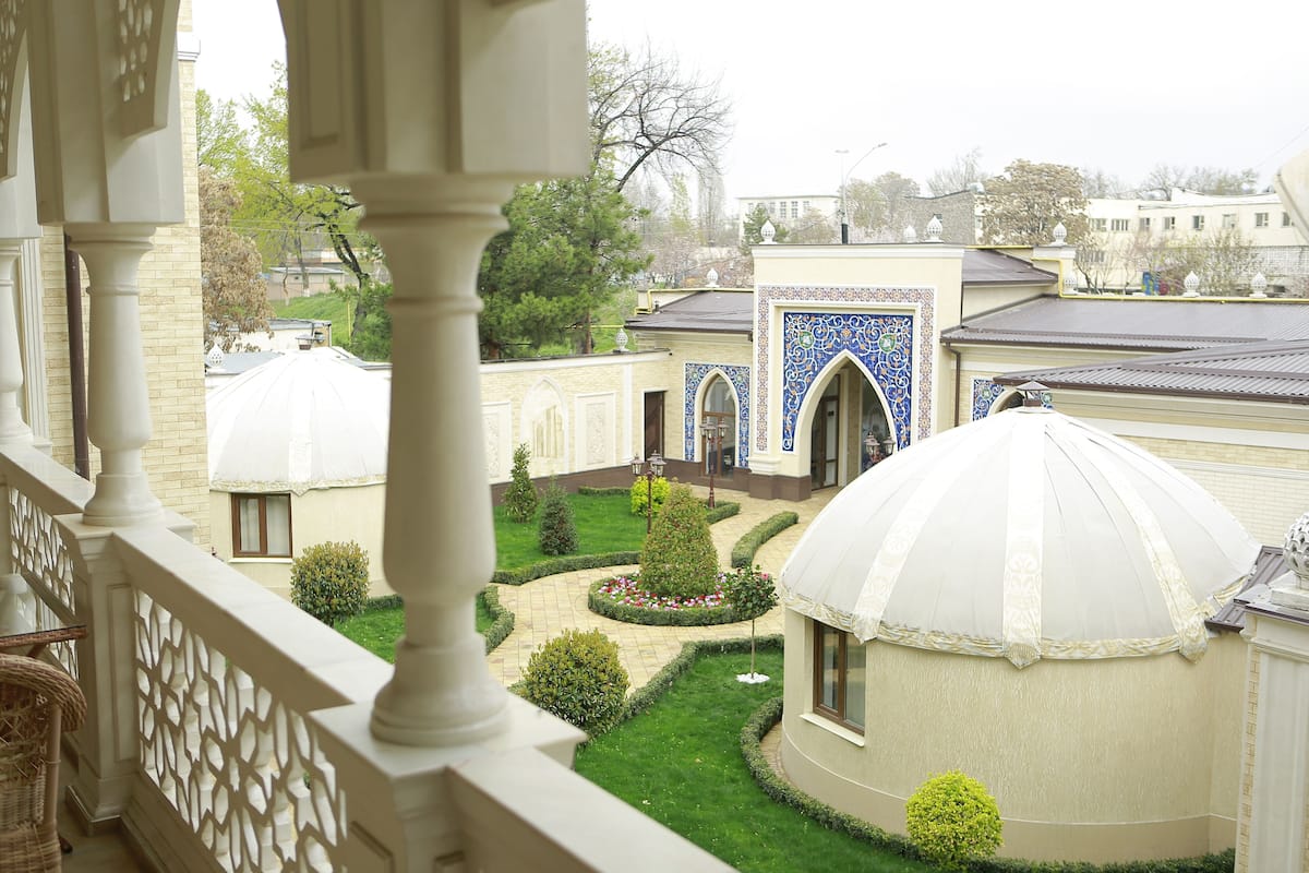 Une cour intérieure dotée d’un dôme central et entourée de bâtiments, avec un jardin aux motifs géométriques et une balustrade blanche.