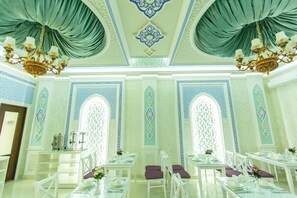 Uma sala de jantar com mesas e cadeiras brancas, paredes com padrão azul e branco e lustres elaborados.
