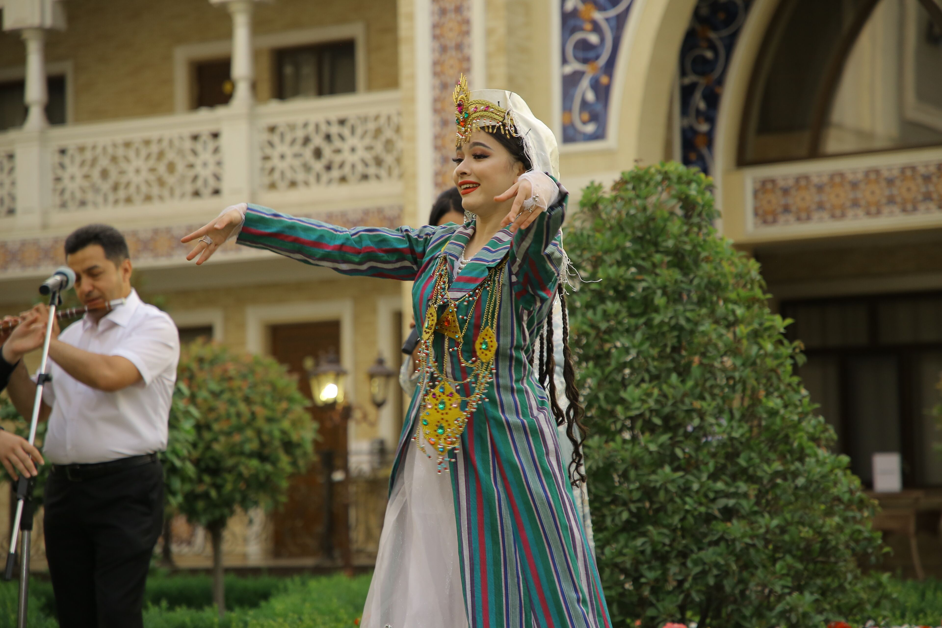 A person in traditional attire performing in front of a building with ornate architecture.