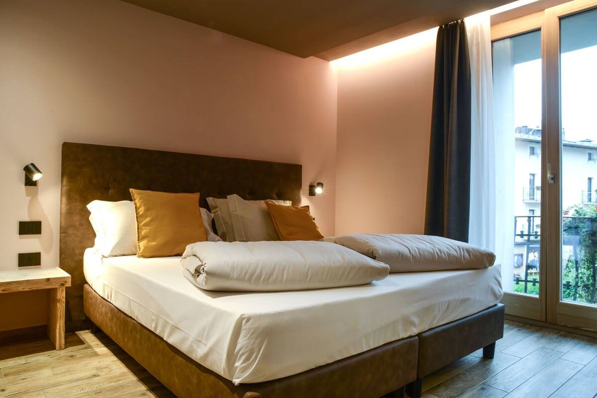 A neatly made bed with white linens and multiple pillows, a wooden headboard, and a nightstand with a lamp.