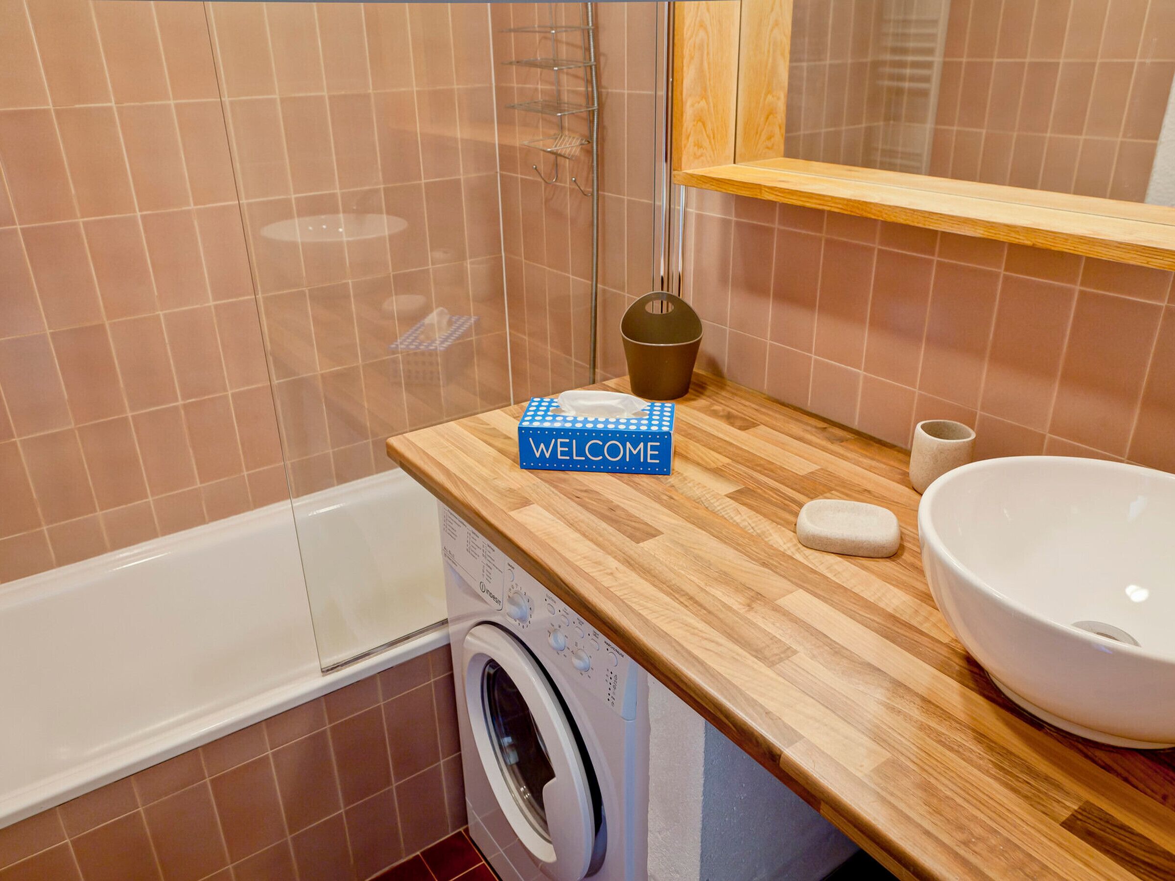 Un baño con encimera de madera, lavadora, lavabo y espejo.