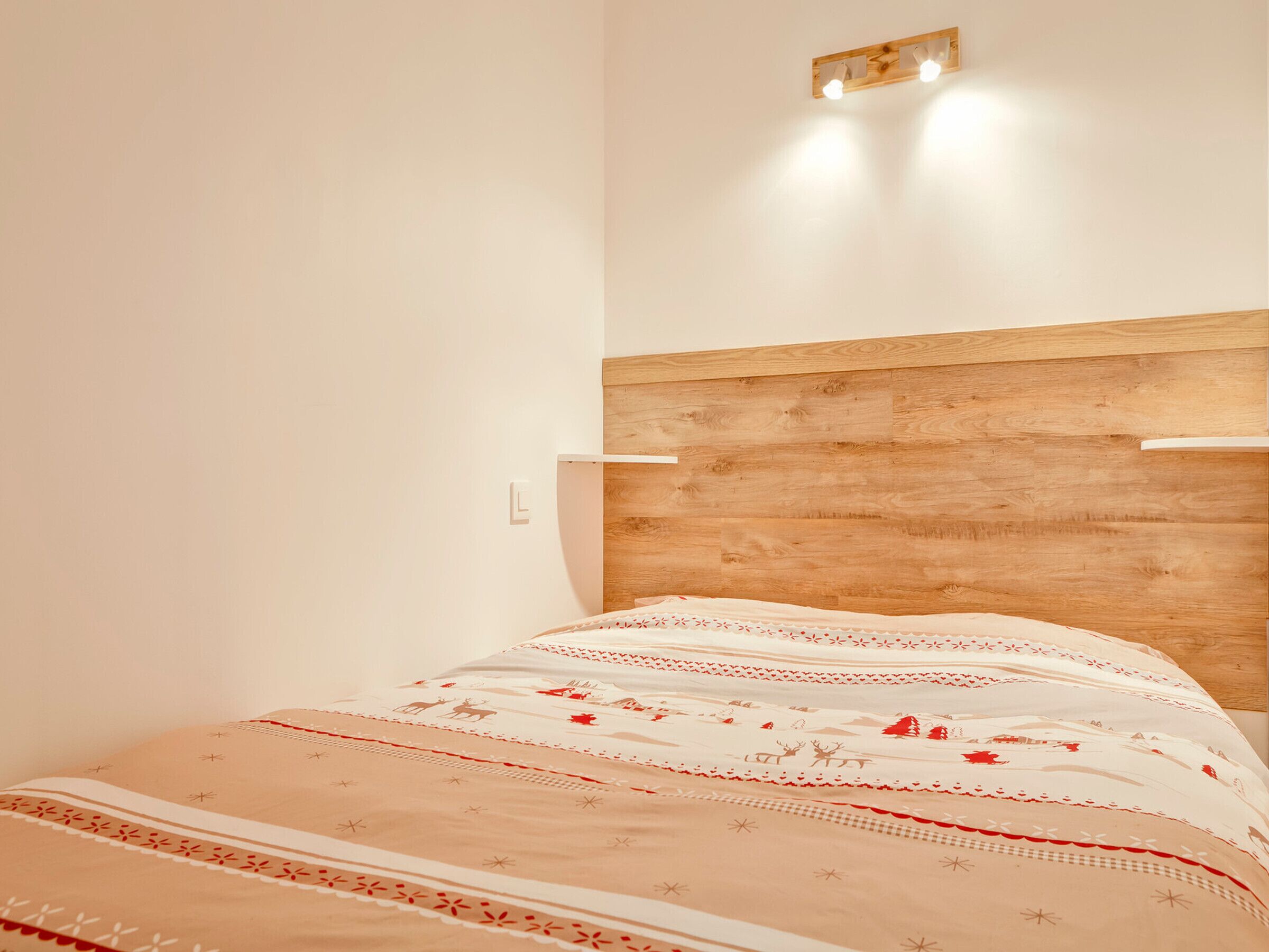 A bed with a wooden headboard, a white wall, and a light fixture above it.