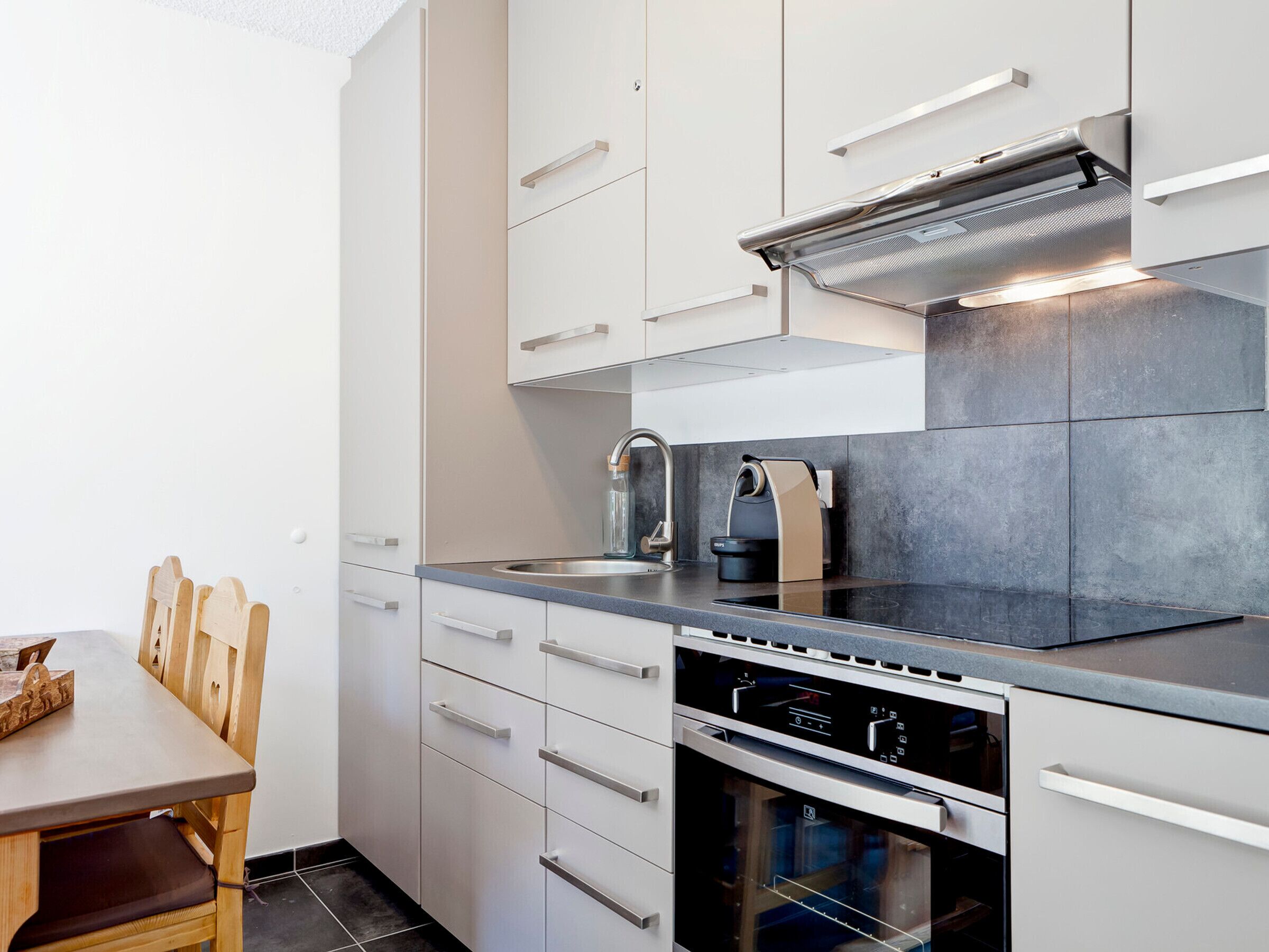 A modern kitchen with white cabinetry, a stainless steel sink, a built-in oven, and a coffee machine.