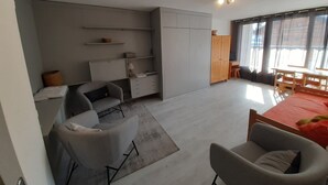 Ein modernes, kompaktes Wohnzimmer mit Küchenzeile, Essbereich und großem Fenster für natürliches Licht.