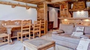 A rustic wooden interior with a dining table set for four, a sofa, and a small wooden table. - Charming apartment in Courchevel 1650 with parking (Courchevel 1650)