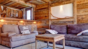 A rustic cabin interior with wooden walls, a wooden table, two sofas, and a large window. - Charming apartment in Courchevel 1650 with parking (Courchevel 1650)