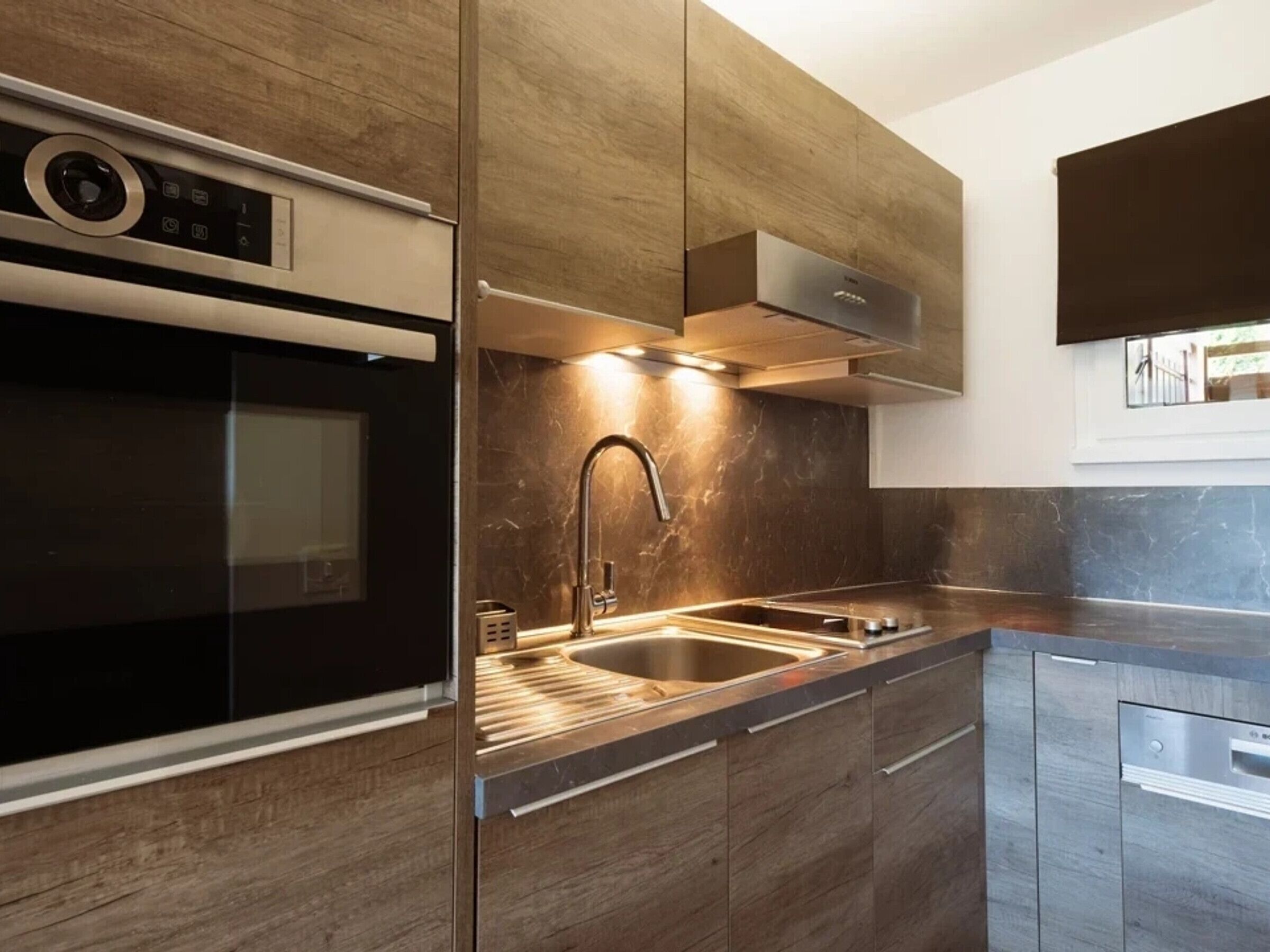 Een moderne keuken met een ingebouwde oven, een roestvrijstalen spoelbak en houten keukenkastjes.