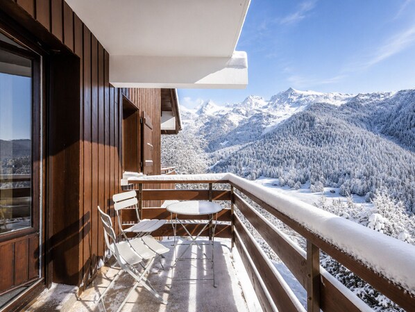 A balcony with a wooden railing overlooking a snowy mountain landscape.