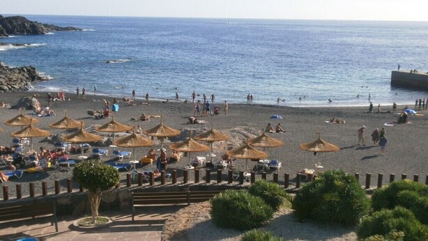 Une plage avec des parasols, des gens et une côte rocheuse.