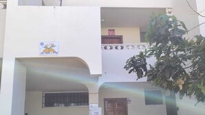 Un bâtiment à deux étages avec une entrée centrale, un petit balcon et un arbre au premier plan.