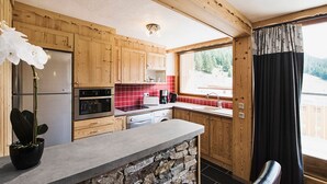 Una cucina con mobili in legno, un piano di lavoro in pietra, un frigorifero, un forno e una finestra con tende.