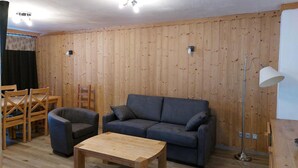 Una stanza con pareti rivestite in legno, un divano grigio, un tavolino in legno, una lampada da terra e un gruppo di sedie in legno.